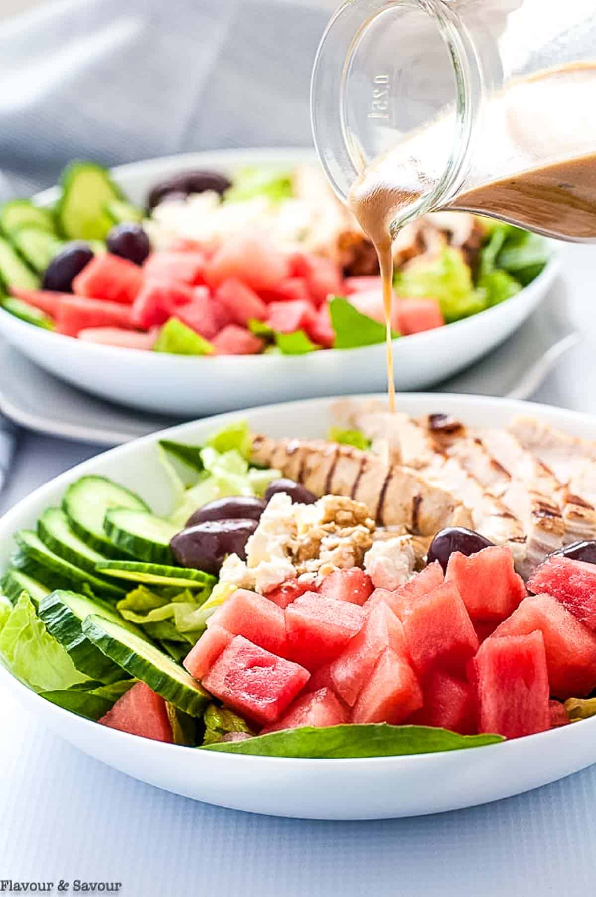 Drizzling balsamic dressing on Greek chicken salad with watermelon and feta.