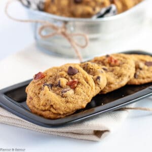 A small black plate with four gluten-free pumpkin pecan chocolate chip cookies.