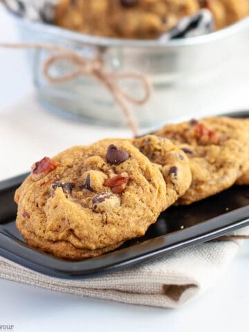 A small black plate with four gluten-free pumpkin pecan chocolate chip cookies.