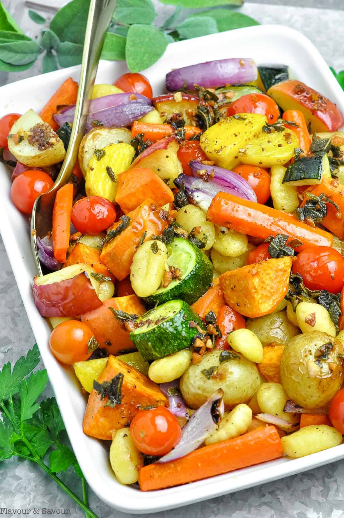 A white serving dish filled with roasted fall vegetables and gluten-free gnocchi, tossed with sage brown butter.