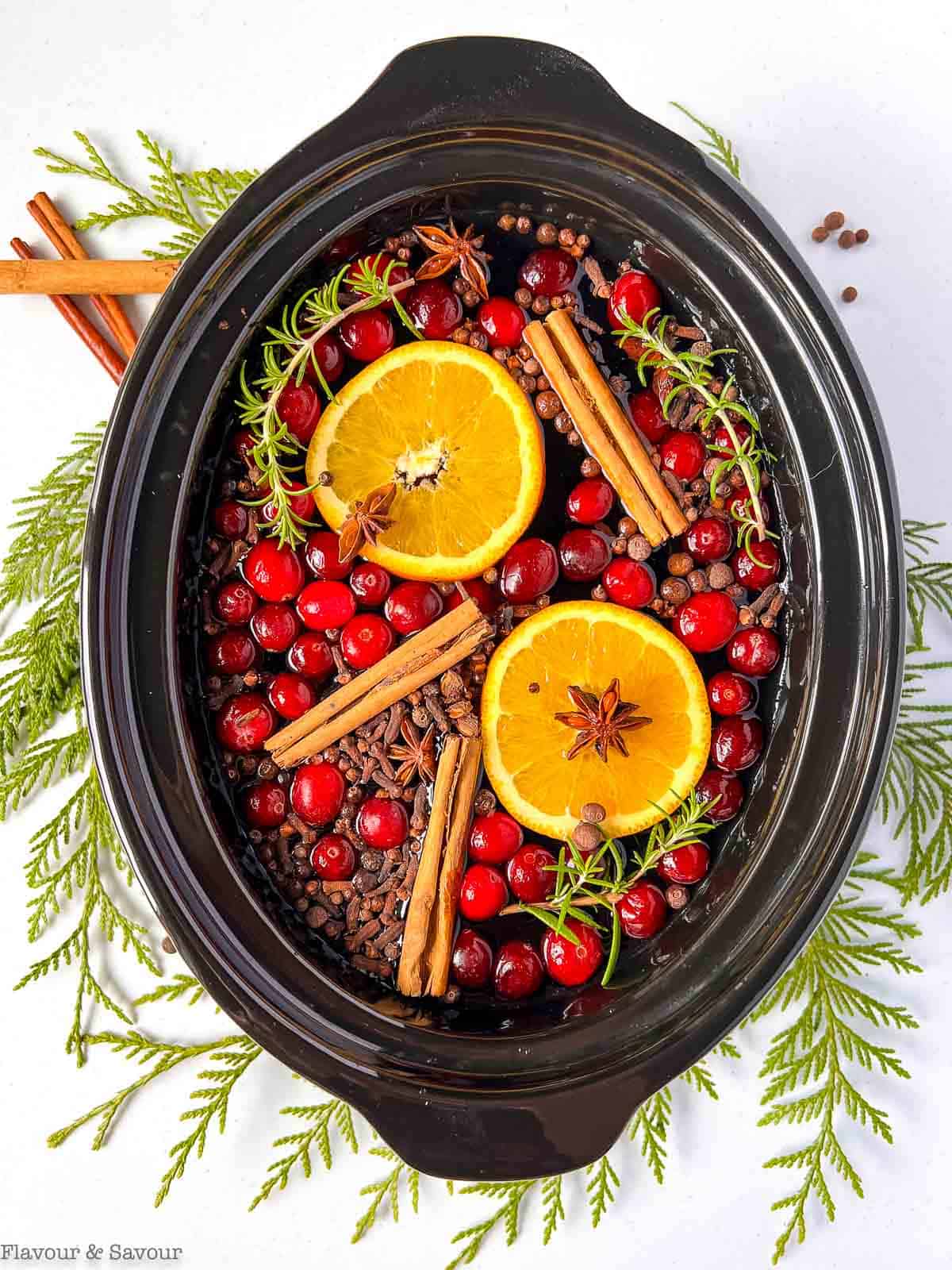 Overhead view of an oval slow cooker bowl with a potpourri spice mix floating in water with oranges and cranberries.