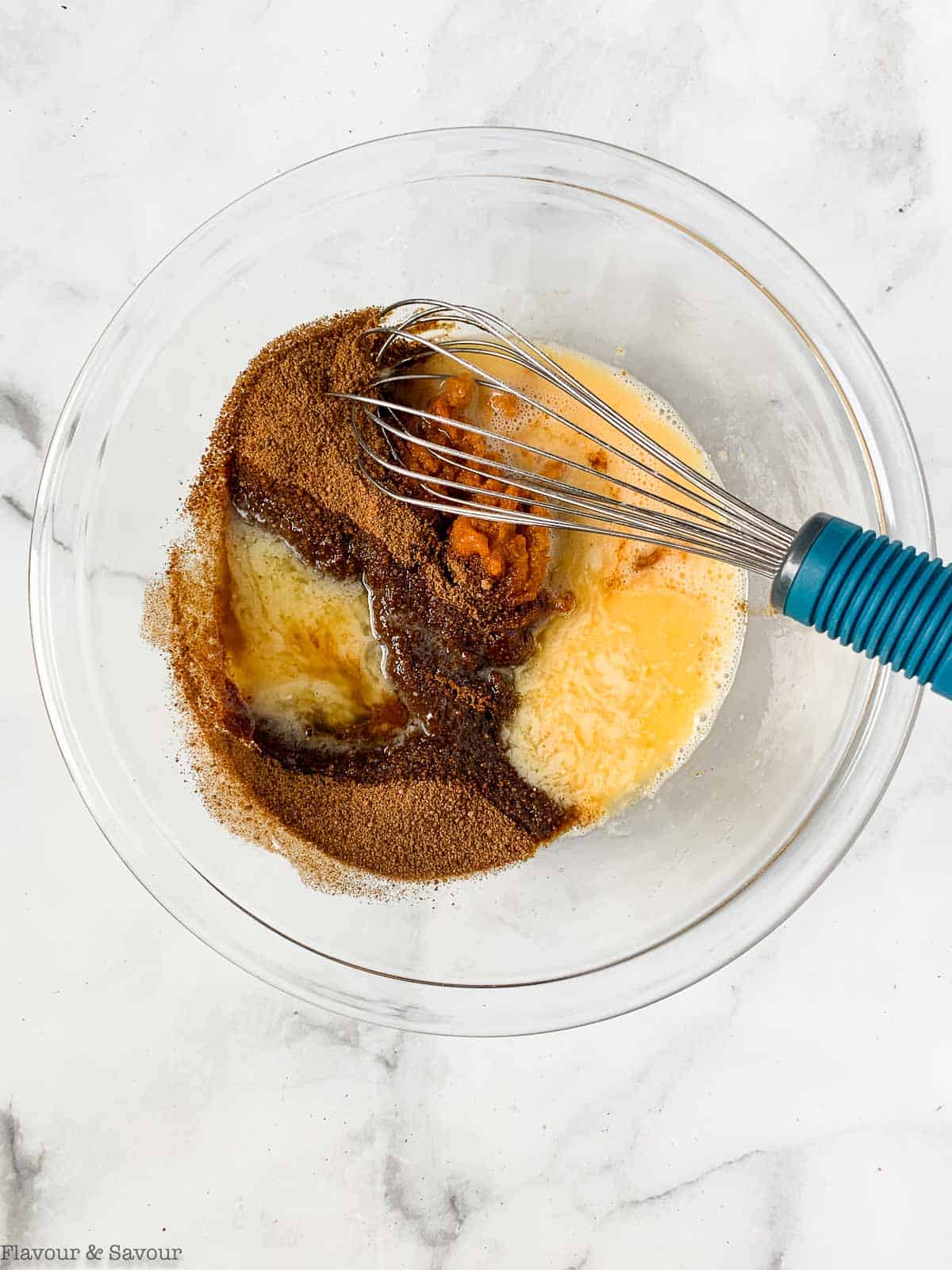 Wet ingredients for gluten-free pumpkin muffins in a glass bowl with a whisk.