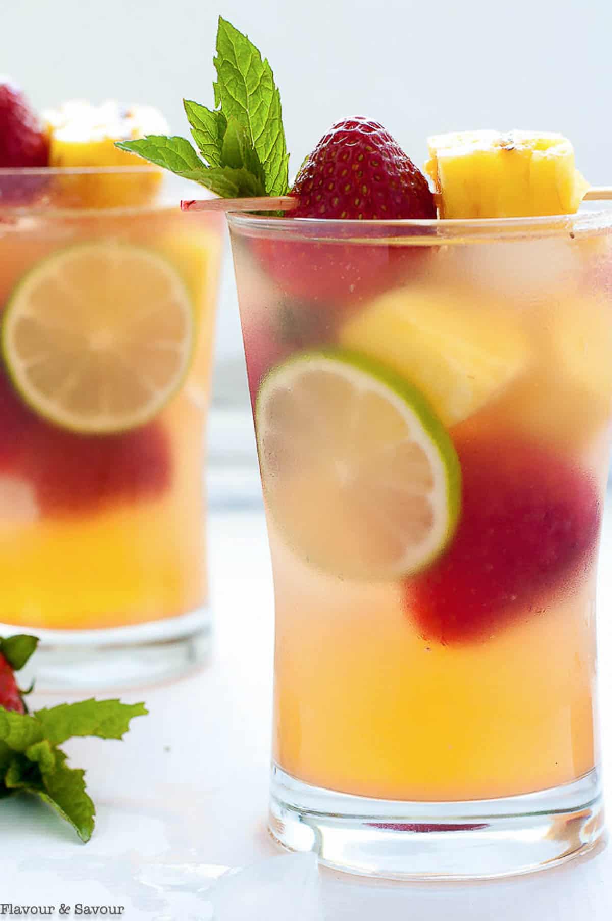 Two glasses of grilled pineapple strawberry sangria garnished with fresh fruit.