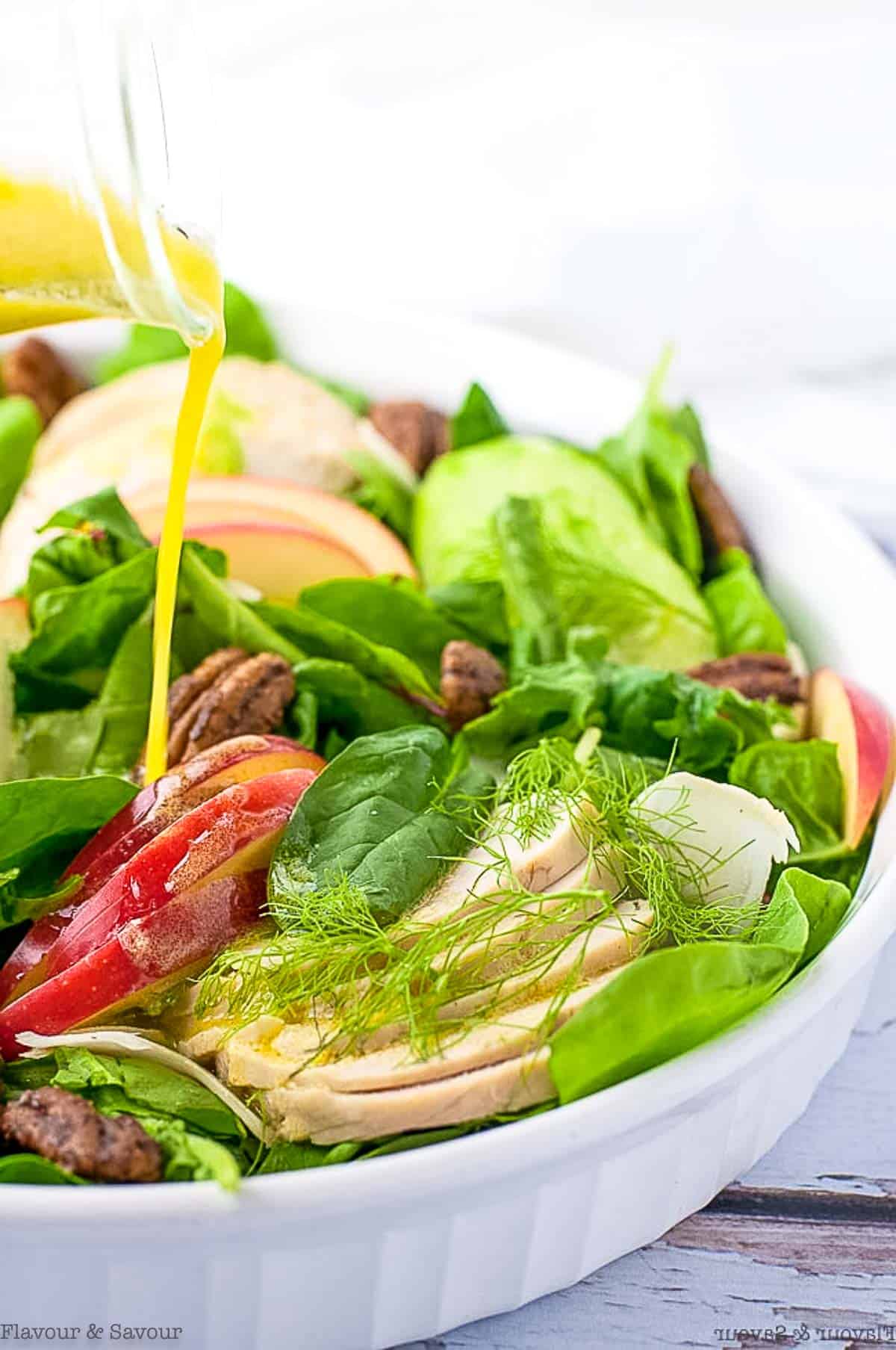 Drizzling dressing on fennel apple chicken salad.