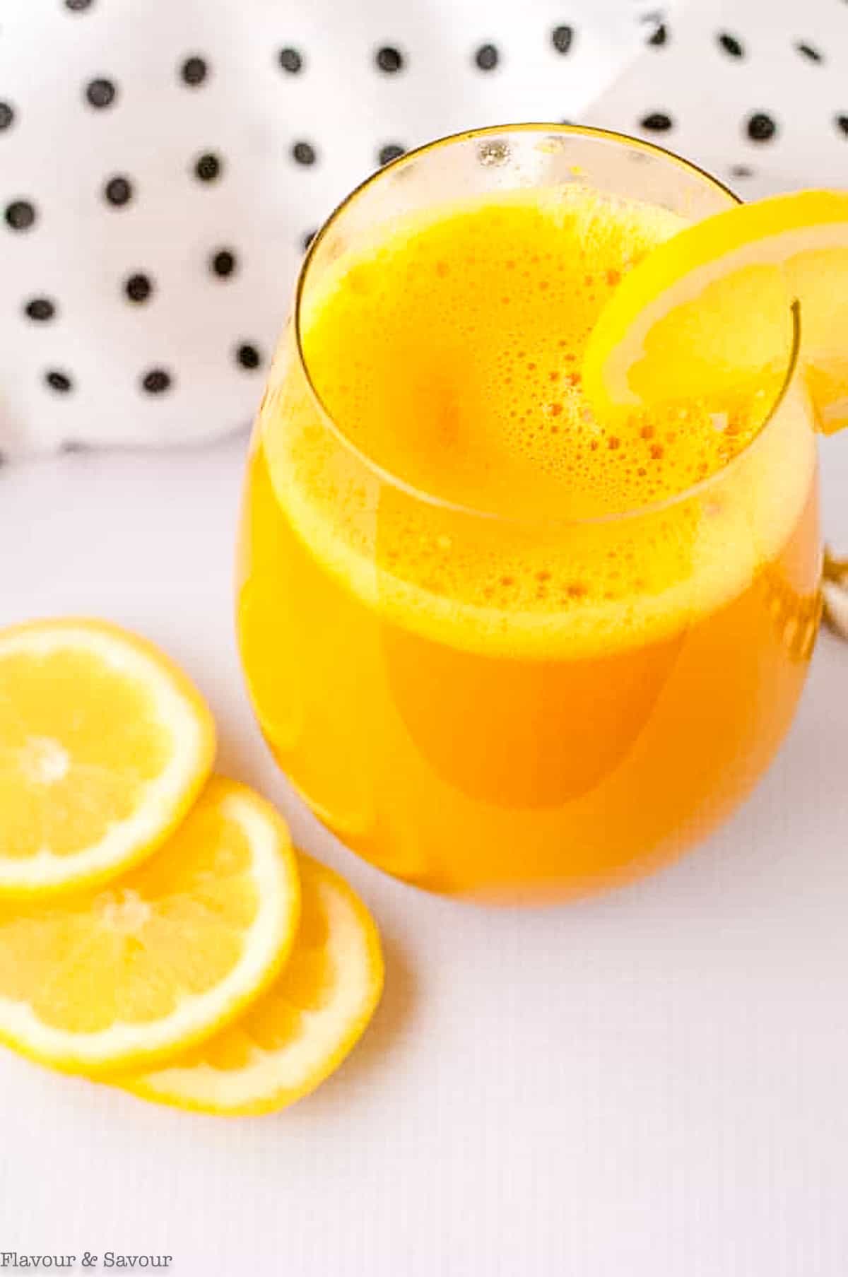 Close up view of a glass of turmeric tonic with lemon slices.