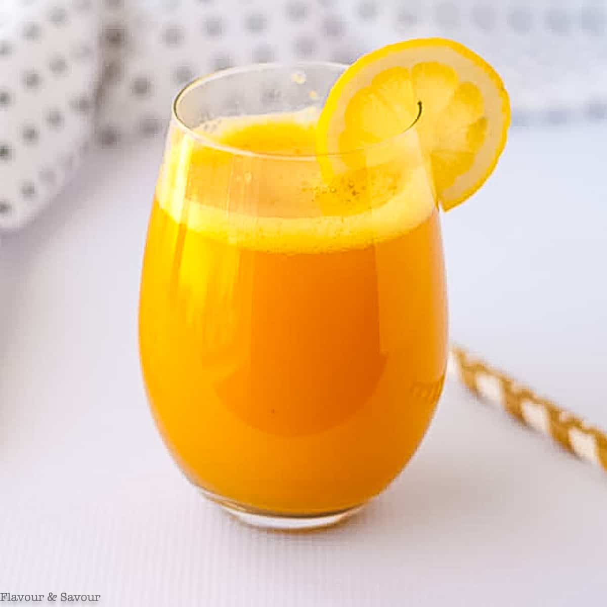A glass of turmeric tonic garnished with a slice of lemon.