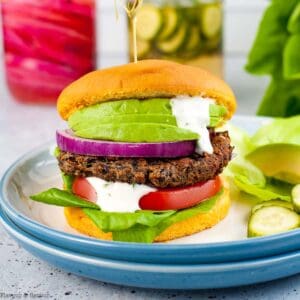 A mushroom black bean burger on a plate garnished with tomato, avocado and lemon aioli.