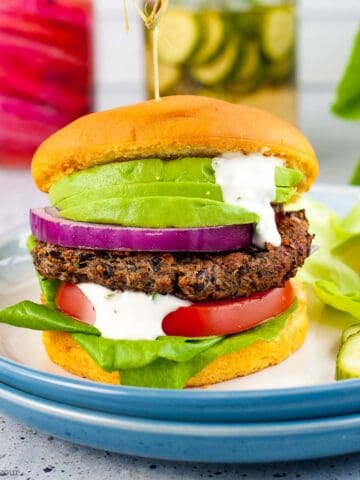 A mushroom black bean burger on a plate garnished with tomato, avocado and lemon aioli.