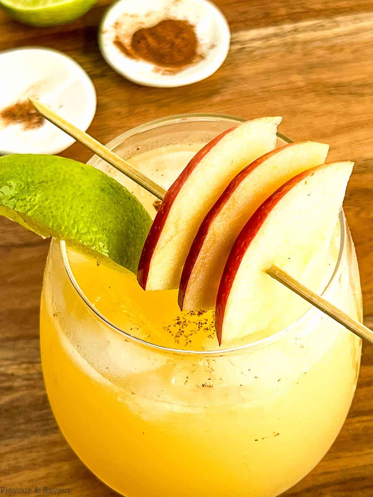 Close up view of a glass of apple cider ginger beer mocktail with apple slices on a cocktail skewer.