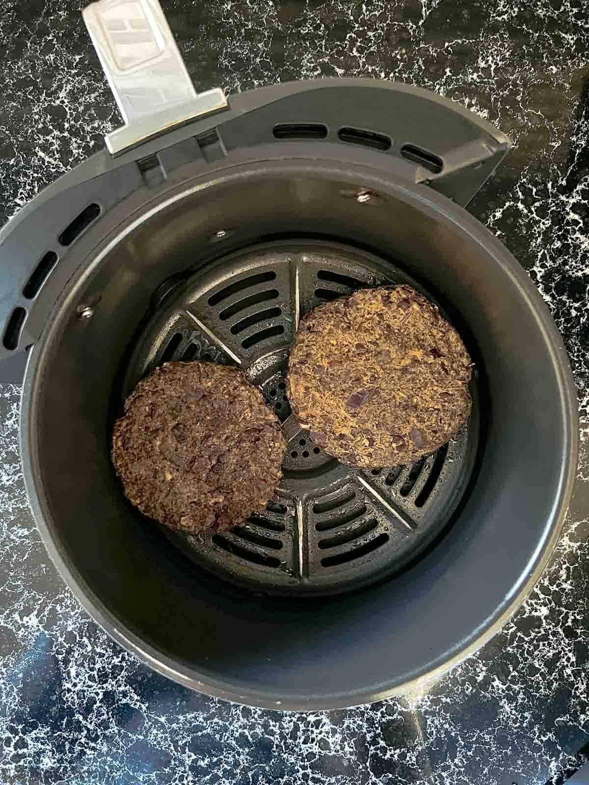 Two black bean burgers in an air fryer.