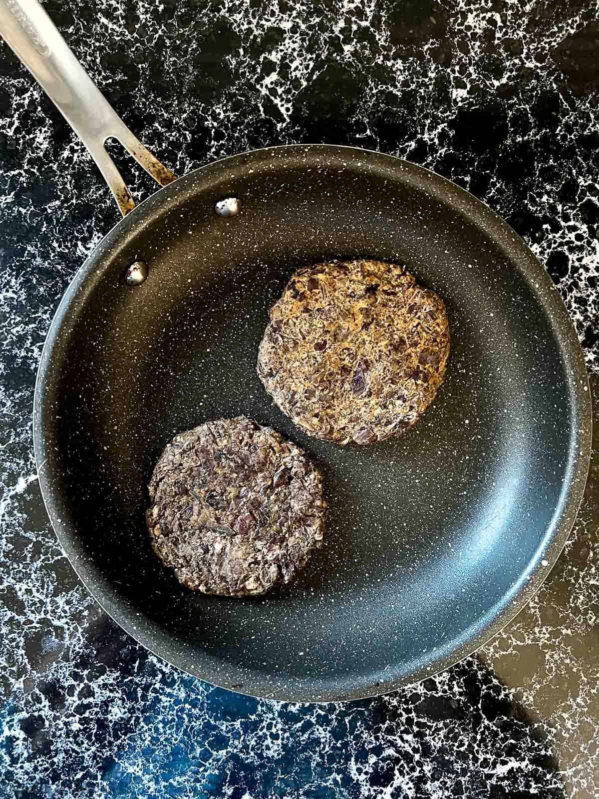 Two black bean burgers in a skillet.