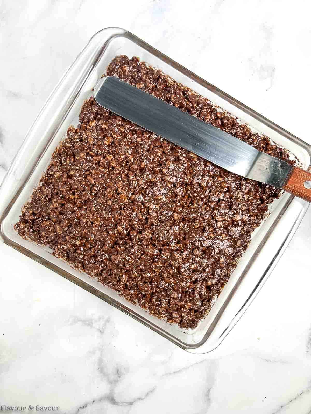 Pressing chocolate peanut butter rice krispie squares mixture into an 8-inch square baking dish.