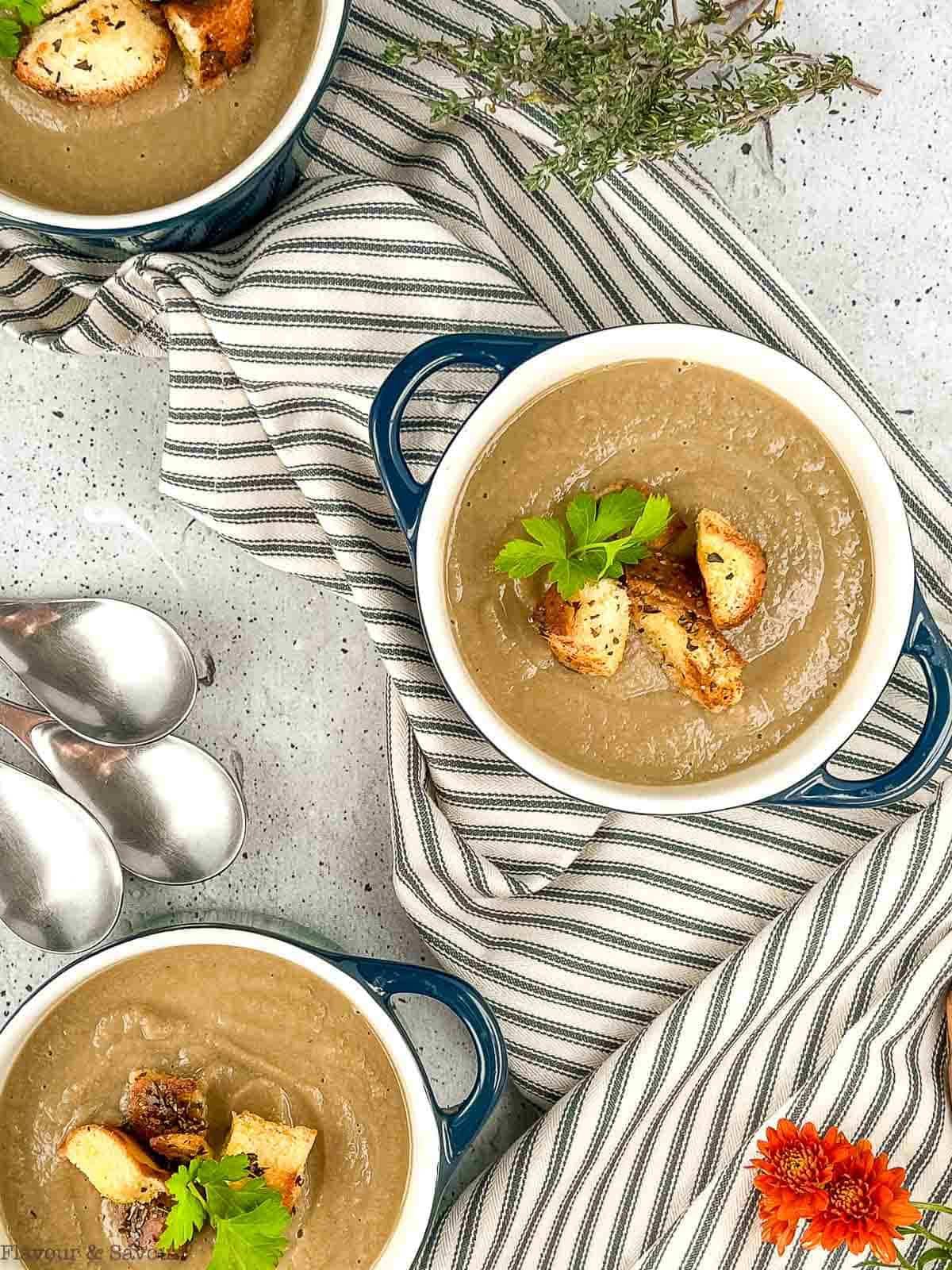 3 bowls of mushroom soup garnished with croutons.