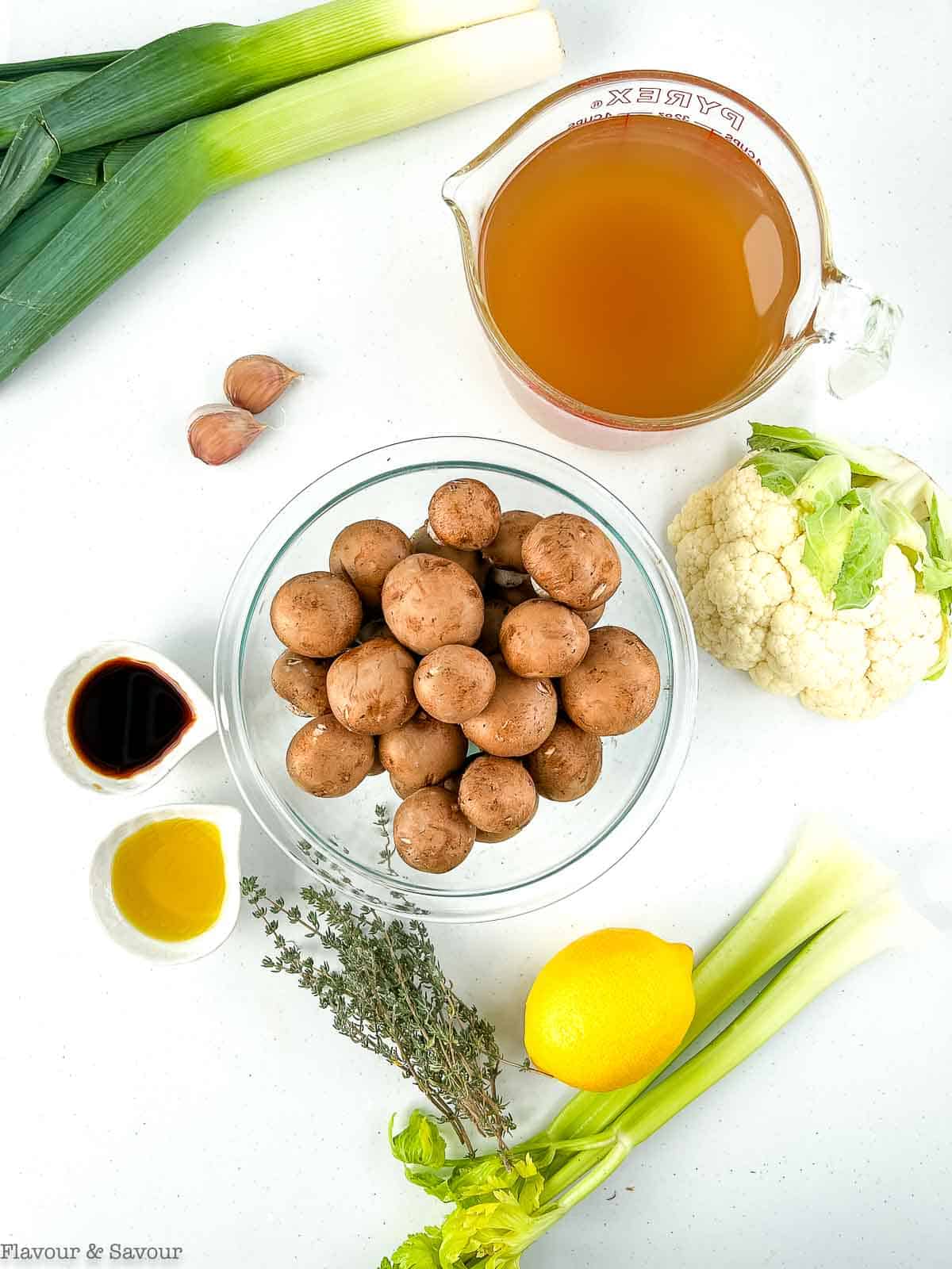 Ingredients for creamy mushroom soup with cauliflower, showing leeks, broth, garlic, mushrooms, thyme, oil, tamari, lemon, celery and cauliflower.