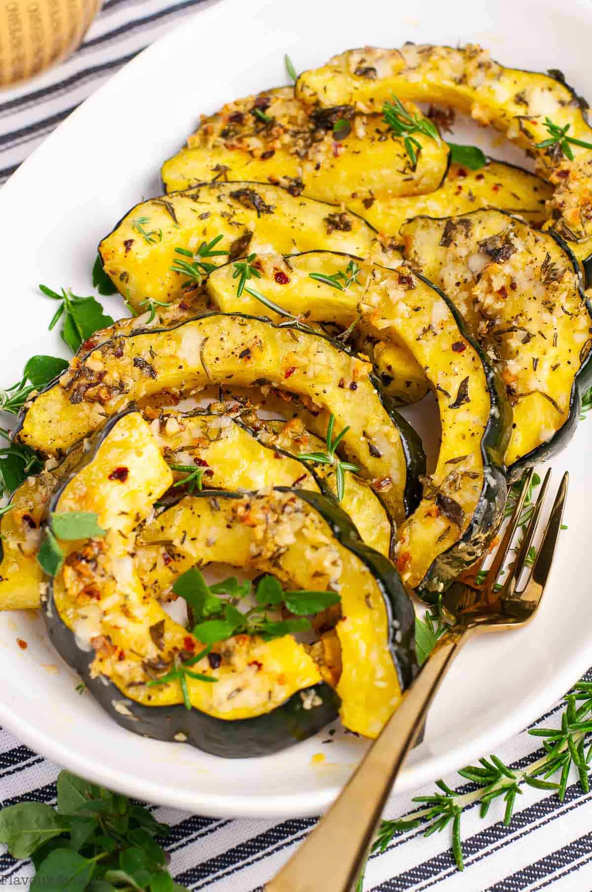 A platter of garlic-parmesan roasted acorn squash slices with fresh herbs.