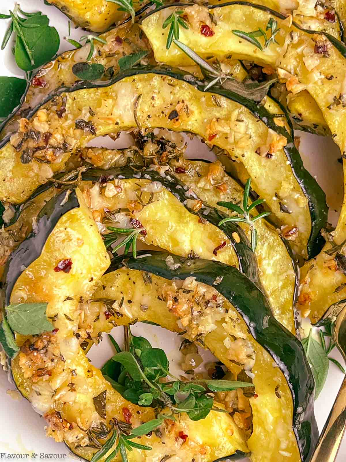 Close up view of slices of roasted acorn squash with garlic, parmesan cheese and fresh herbs.