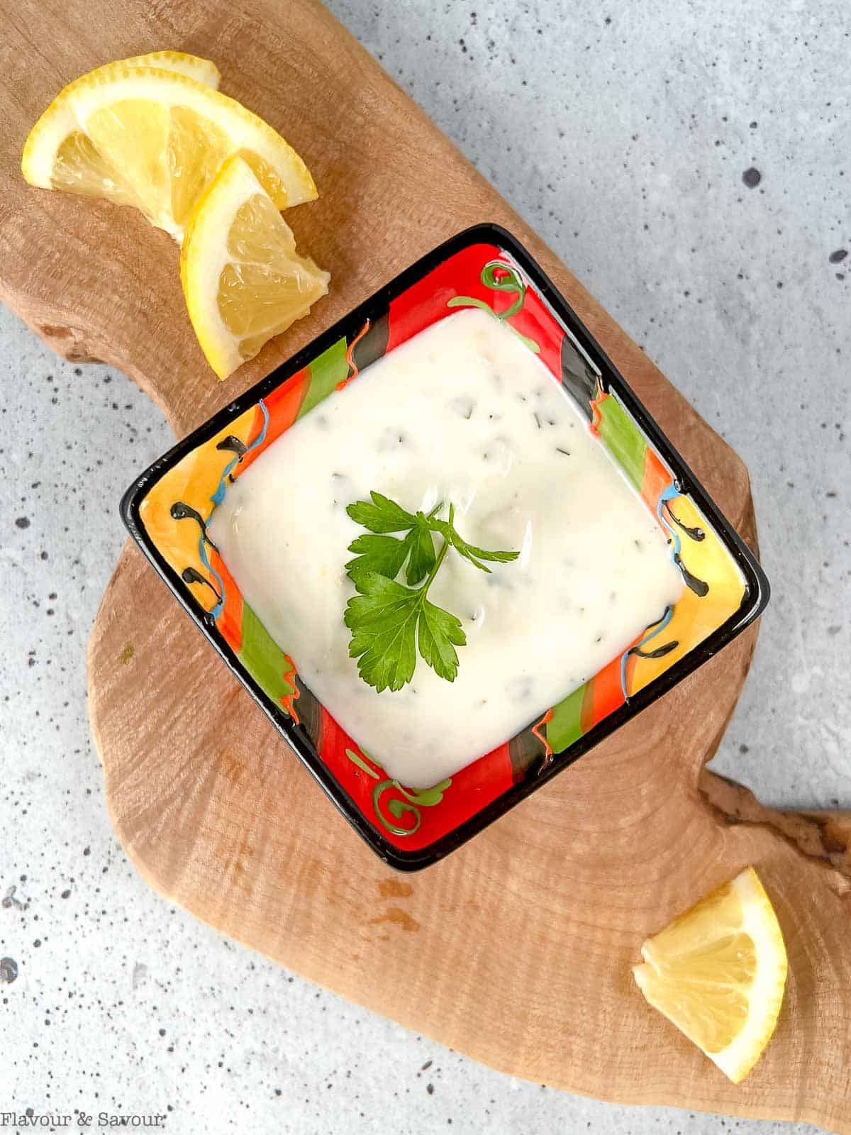 A small square dish of lemon aioli with a sprig of parsley.