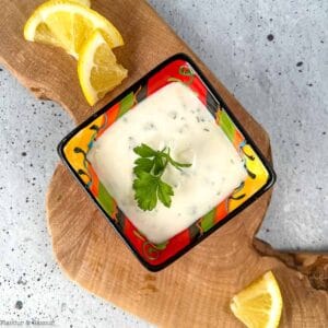 Overhead view of a small bowl of lemon aioli with lemon slices beside it.