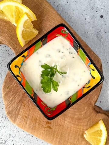 Overhead view of a small bowl of lemon aioli with lemon slices beside it.