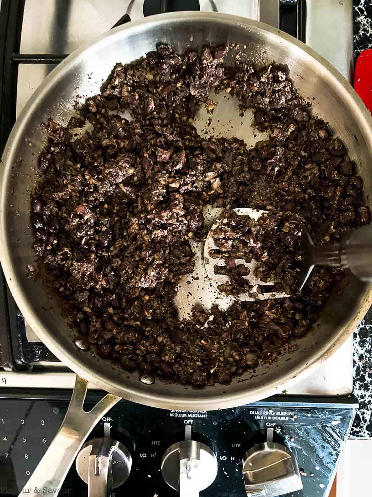 Mashing black beans with mushrooms in a skillet.