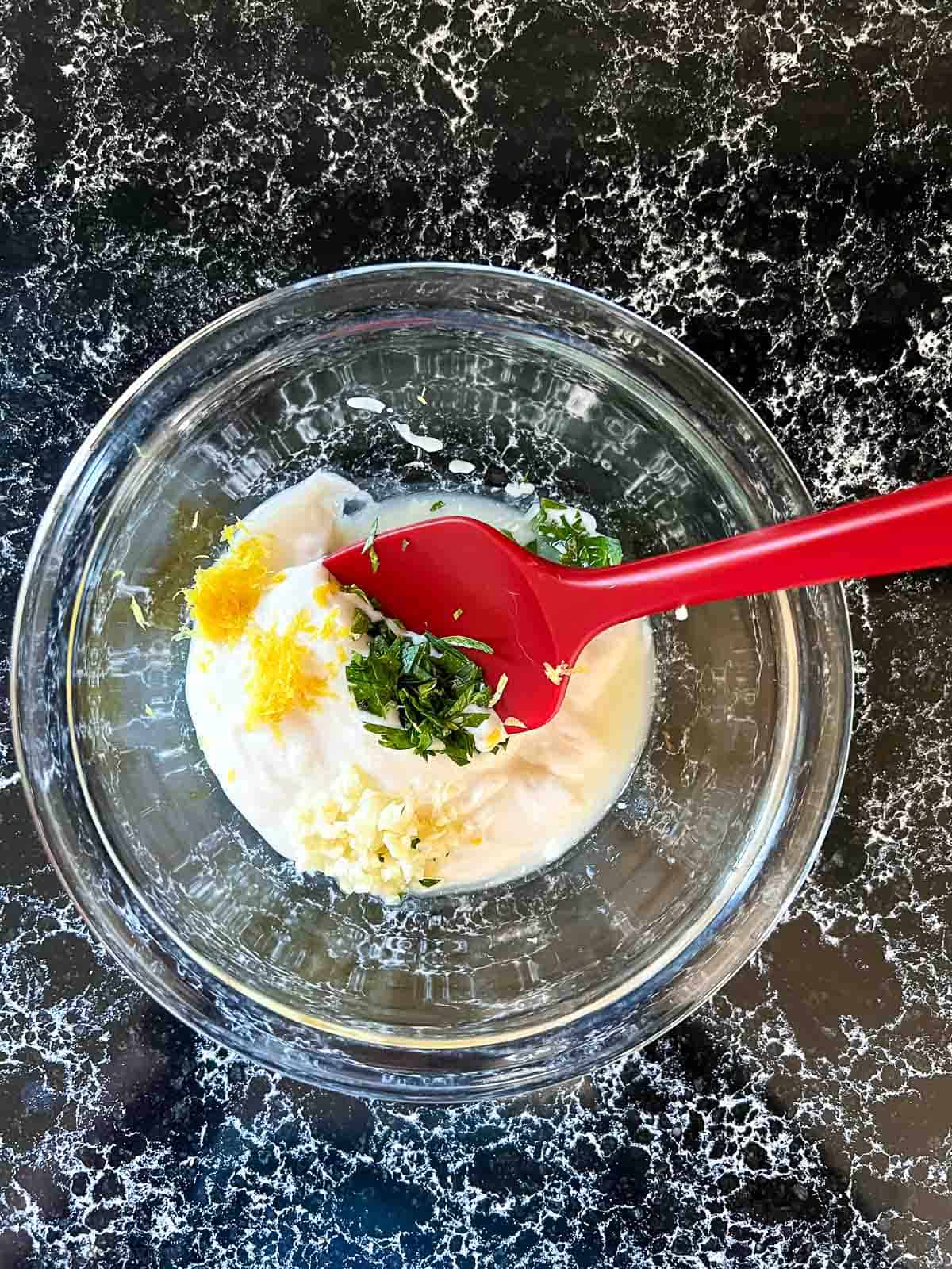 Combining lemon aioli ingredients in a bowl with a spatula.