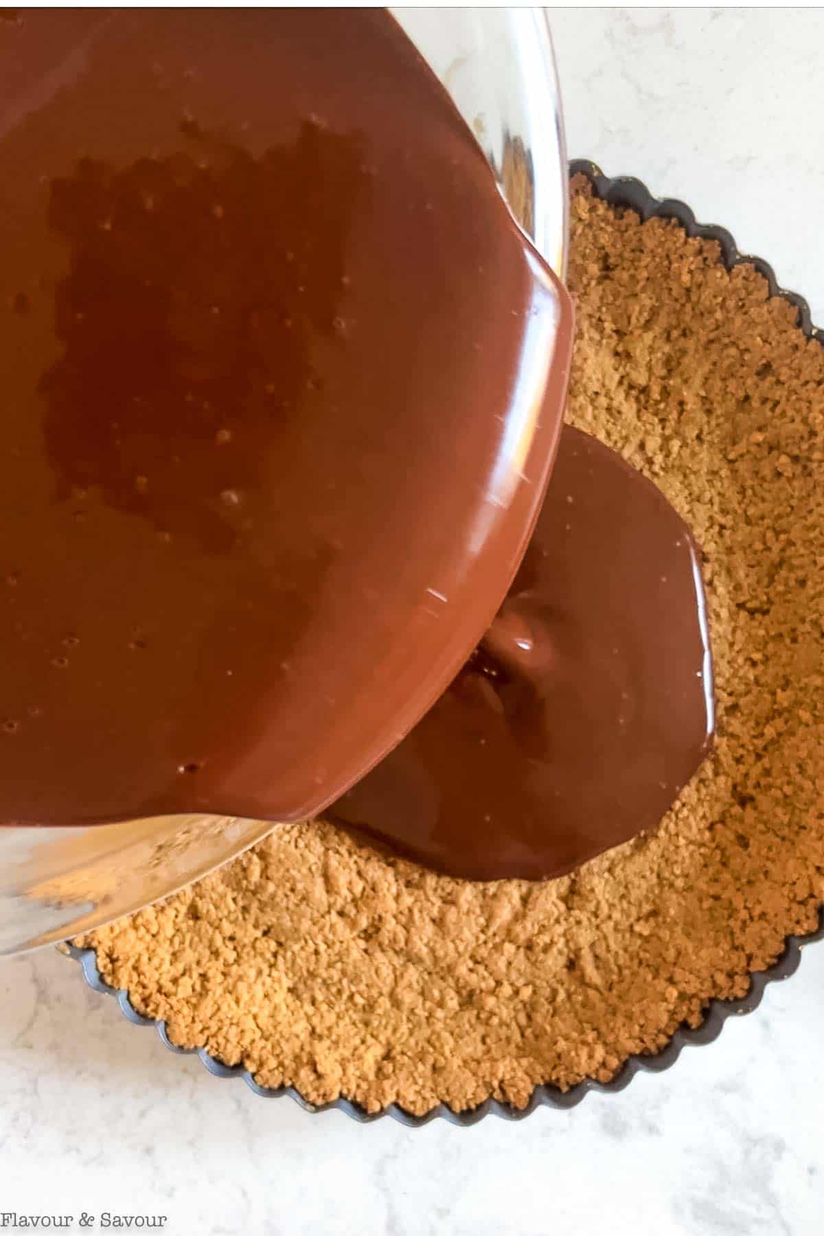 Pouring chocolate-coconut cream mixture into a graham cracker crust to make a vegan chocolate pie.