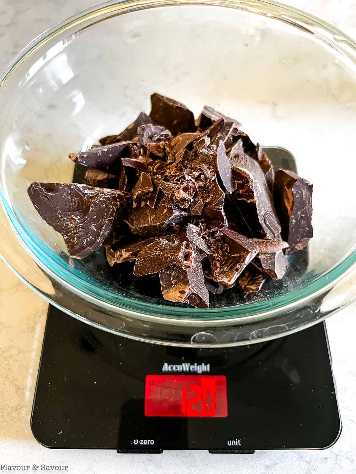 Chopped chocolate in a glass bowl on a digital scale showing 12.0 oz.