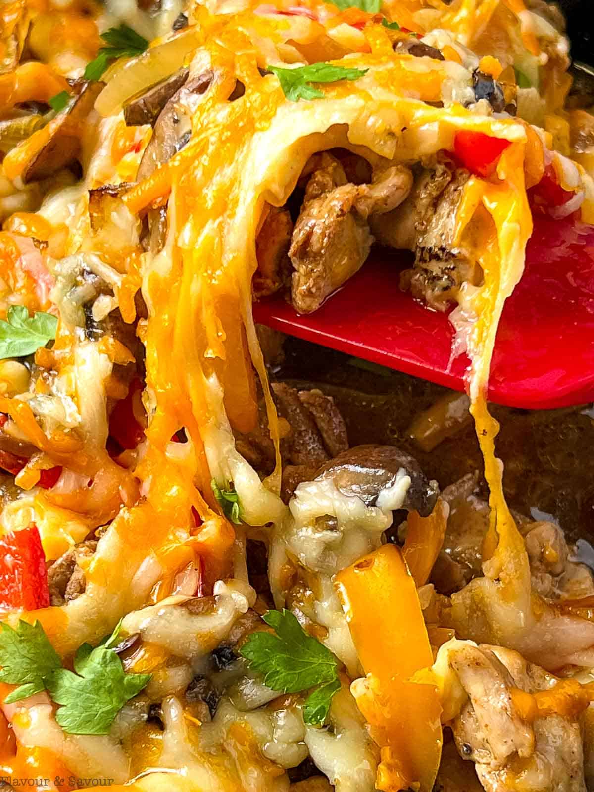 Melted cheese over baked chicken pieces, peppers, onions and mushrooms in a spoonful of baked chicken fajita casserole.