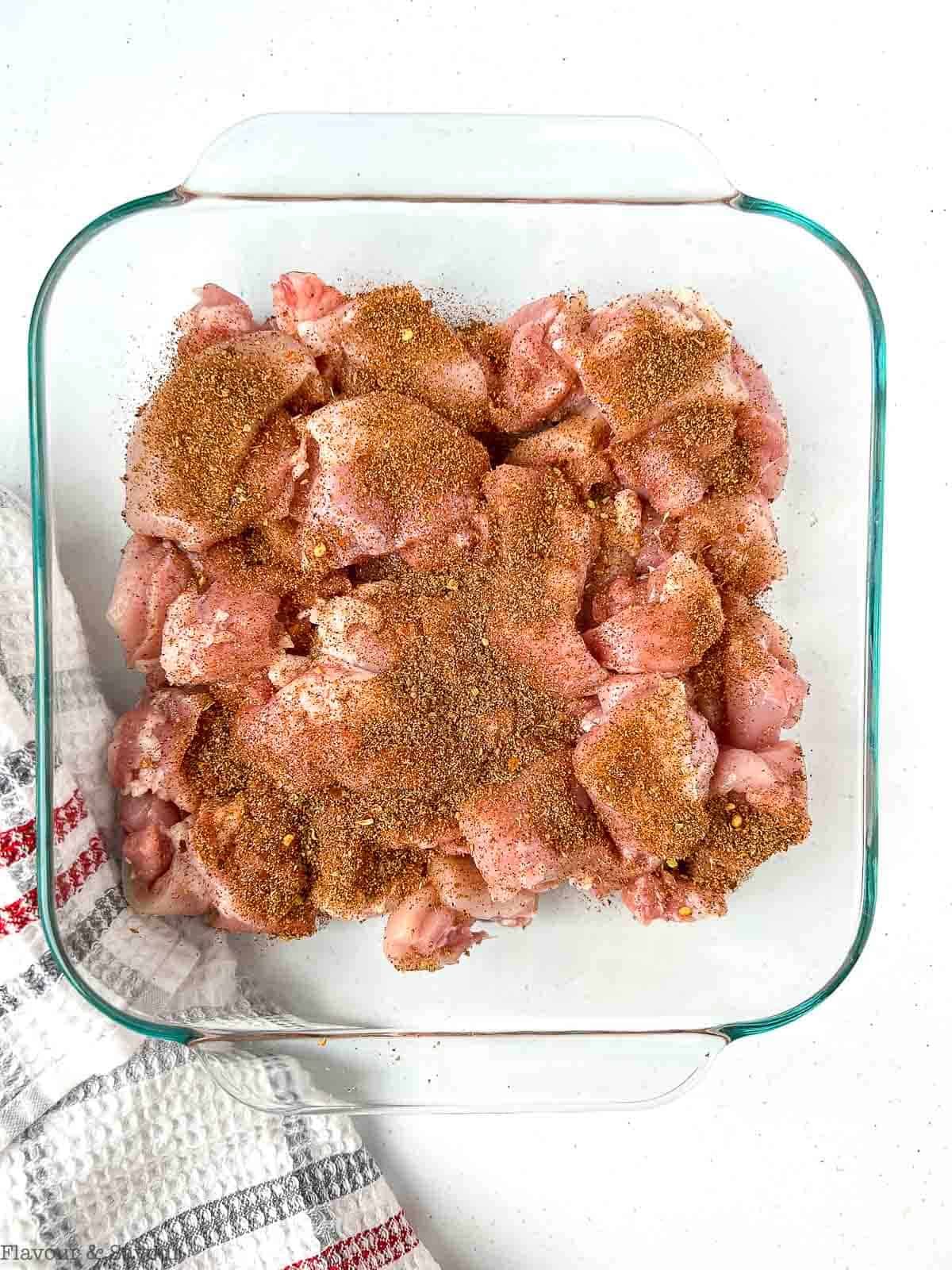 Cubed chicken thighs tossed with fajita seasoning mix in a glass pan.