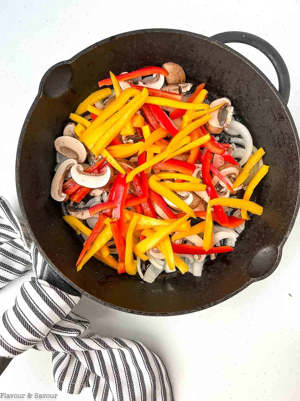 Sliced peppers, onions, and mushrooms in a cast iron skillet.