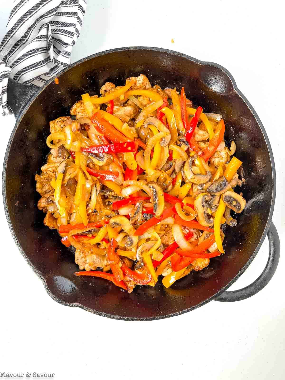 Sautéd peppers and onions on top of browned chicken in a cast iron skillet.