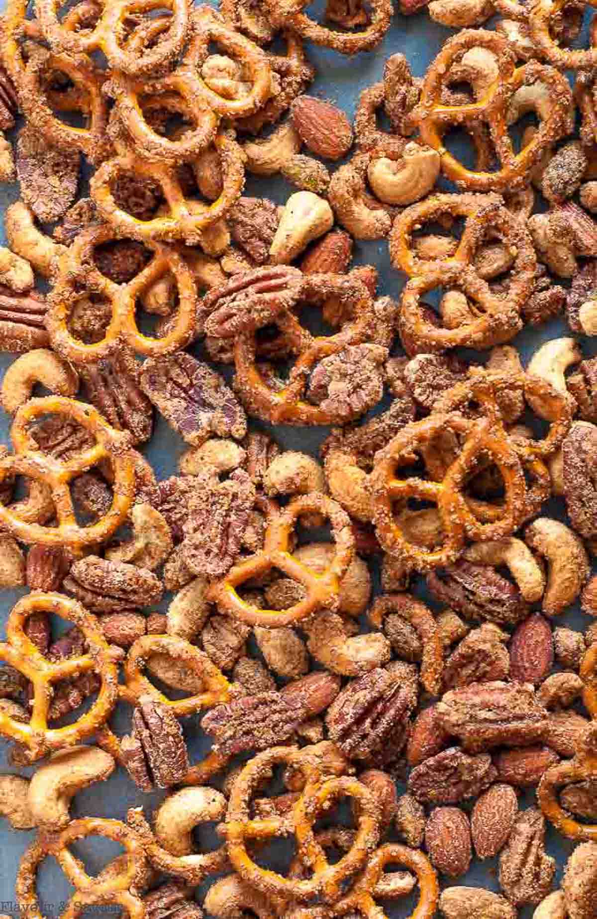 Close up view of a baking tray full of a snack mix made with pretzels and mixed nuts.