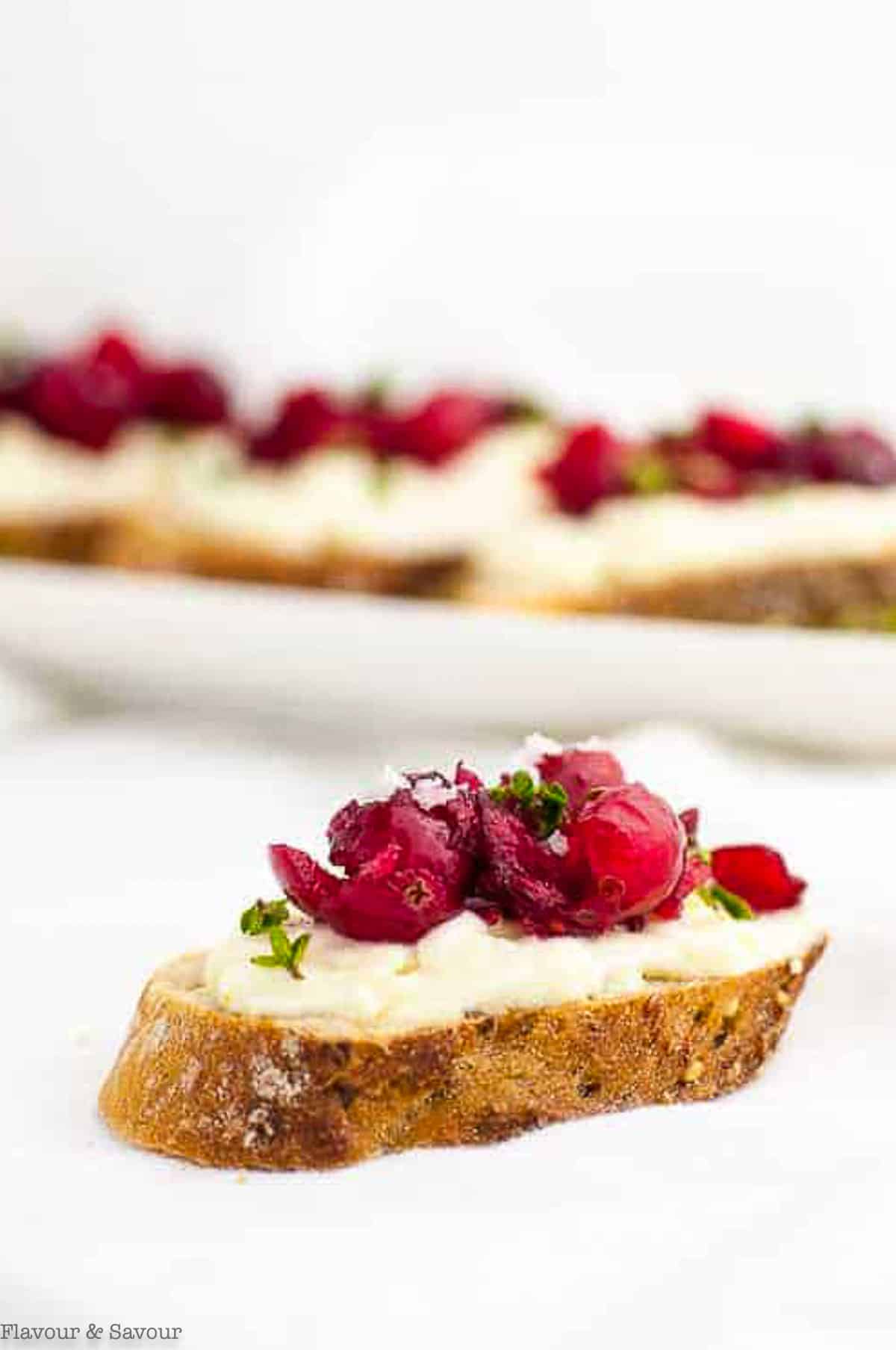 Close up view of a slice of toasted baguette topped with whipped ricotta cheese and fresh, sweetened cranberries.