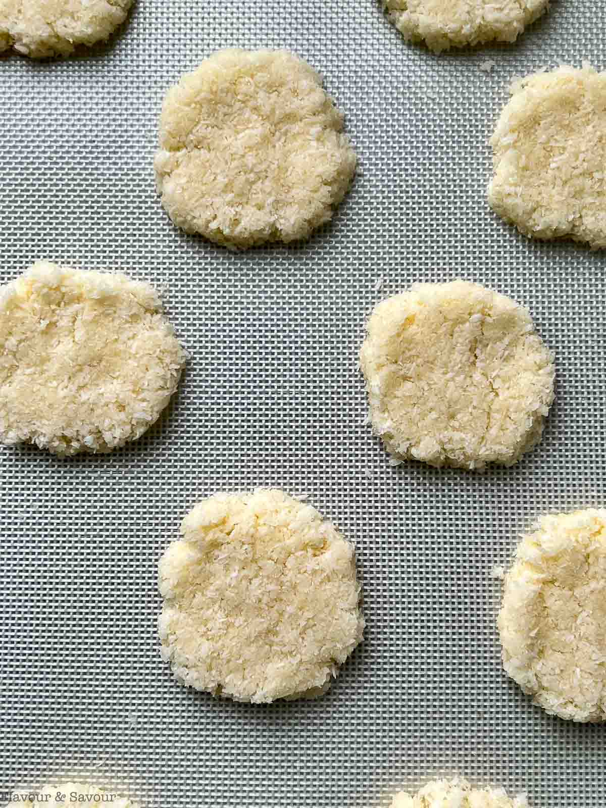 Flattened coconut cookies on a baking sheet.