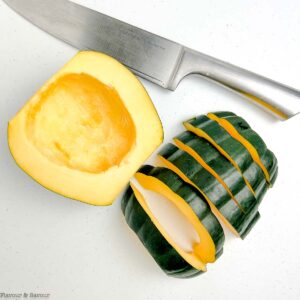 An acorn squash cut in half with one half cut into slices.