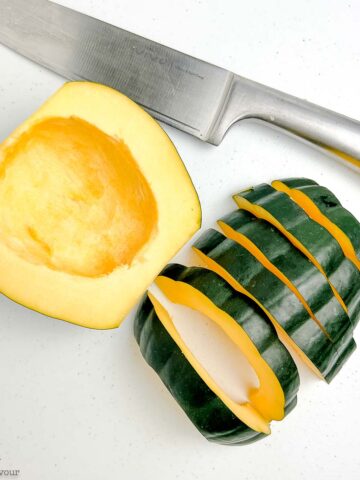 An acorn squash cut in half with one half cut into slices.