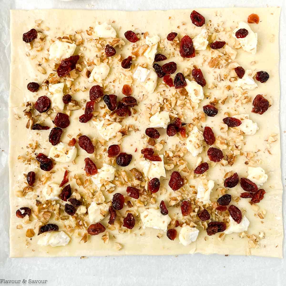A sheet of puff pastry sprinkled with brie, cranberries and walnuts.