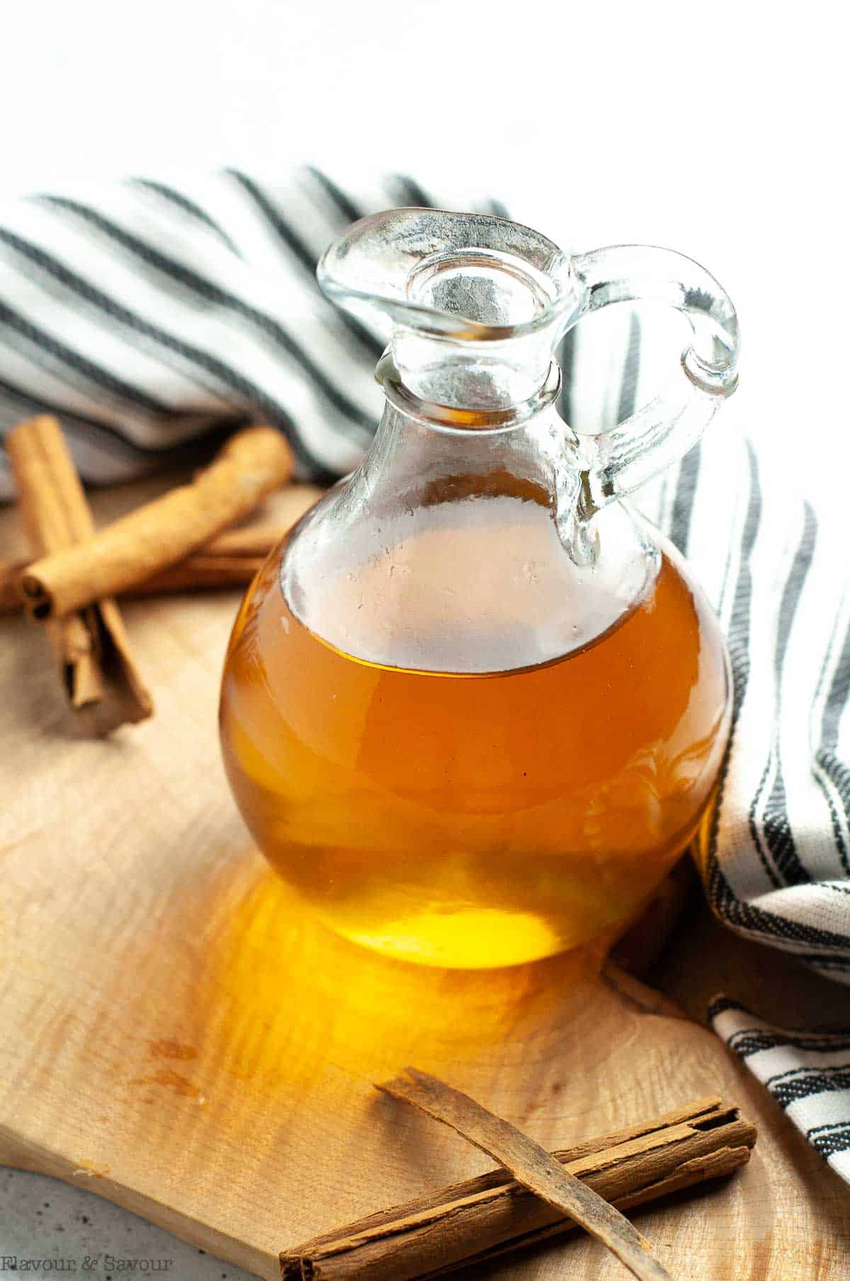 A cruet filled with cinnamon simple syrup with cinnamon sticks nearby.