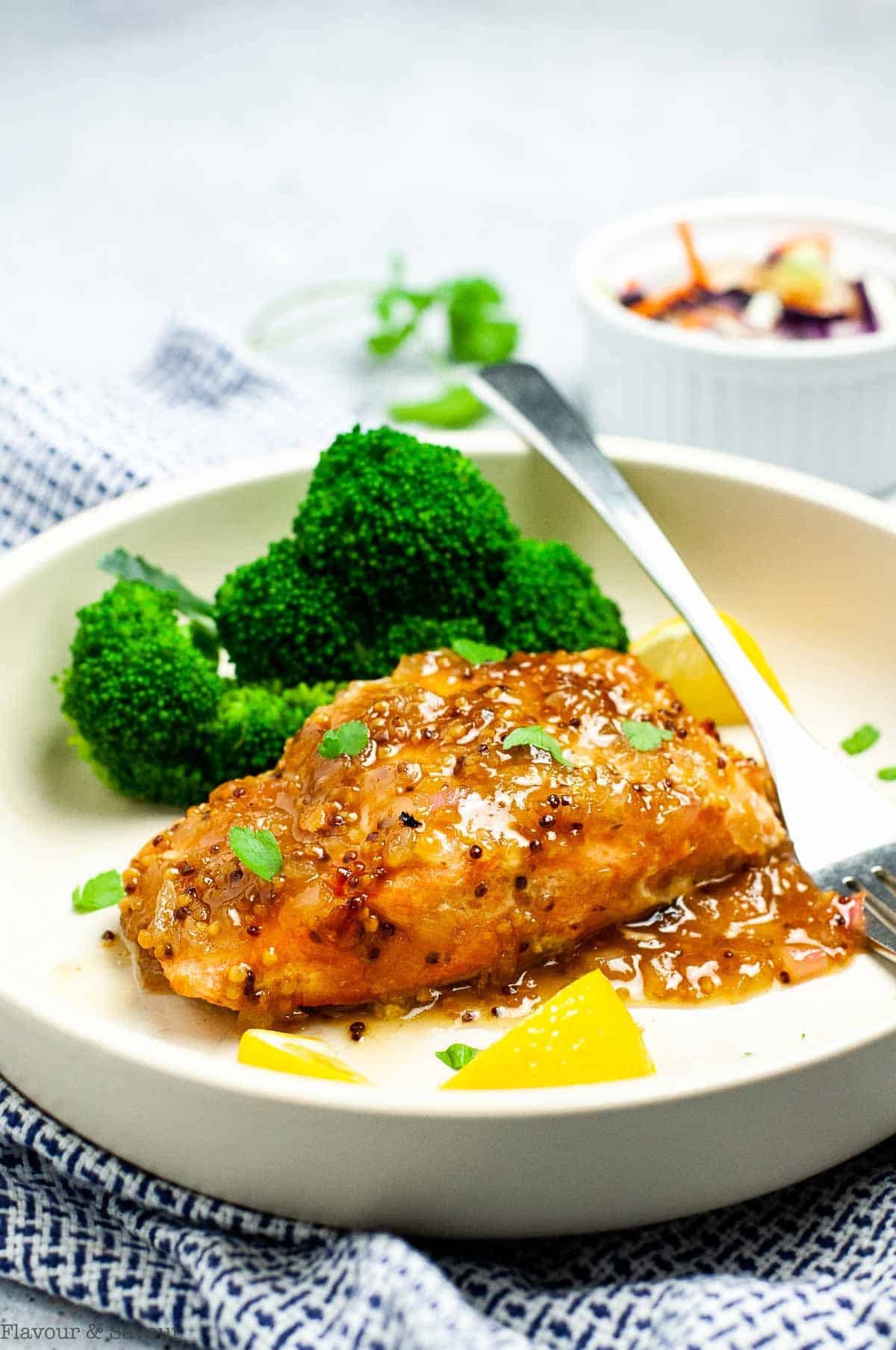 A filet of honey-mustard salmon on a plate with broccoli and lemon wedges.