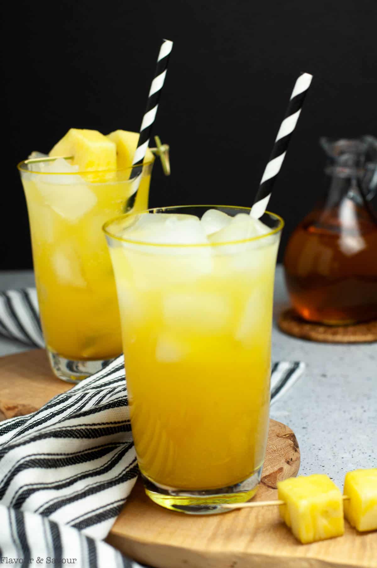 Two glasses of pineapple ginger beer mocktail with striped straws.