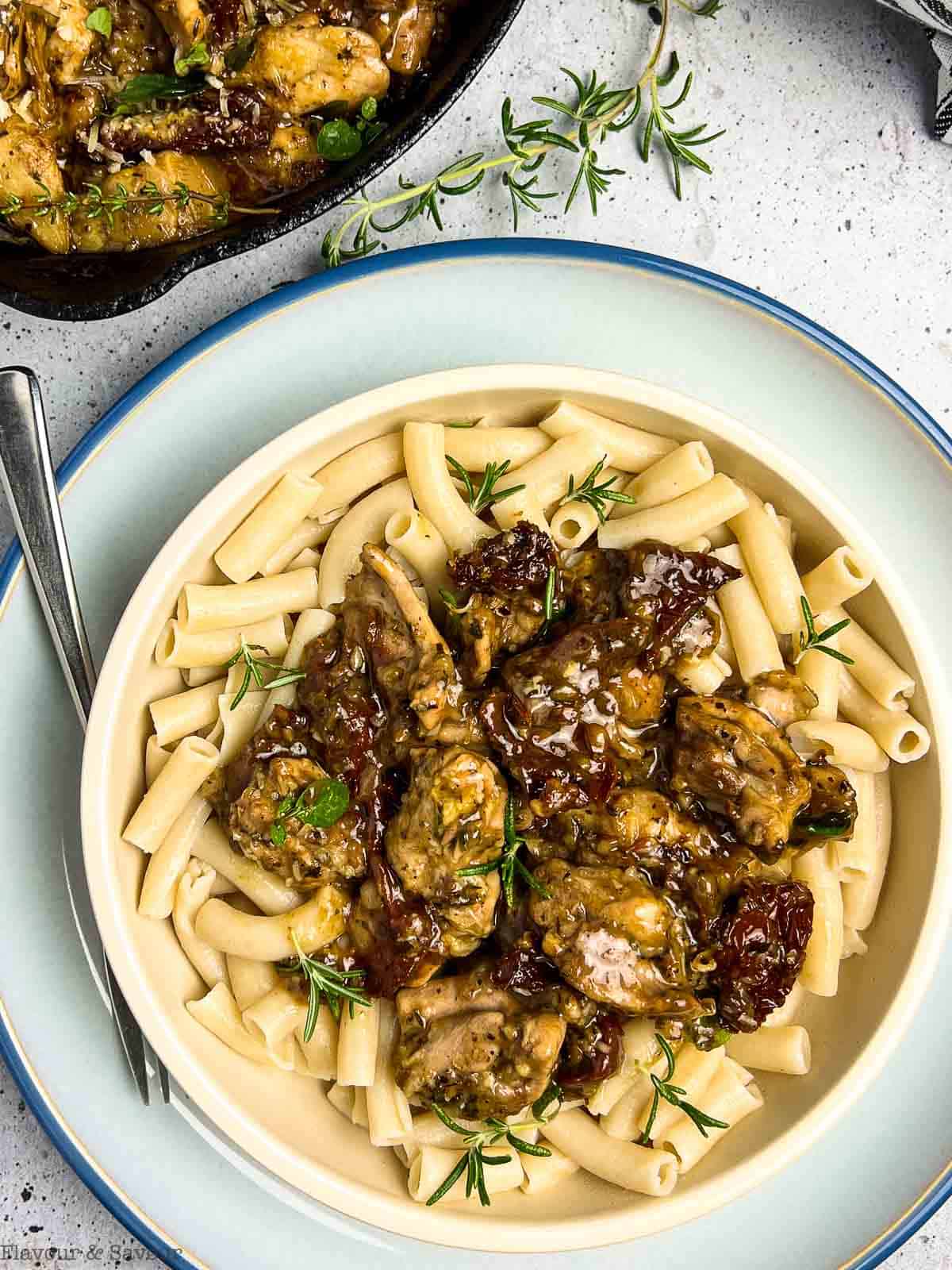 Close up view of a bowl of pasta with sun-dried tomato and artichoke chicken on top.