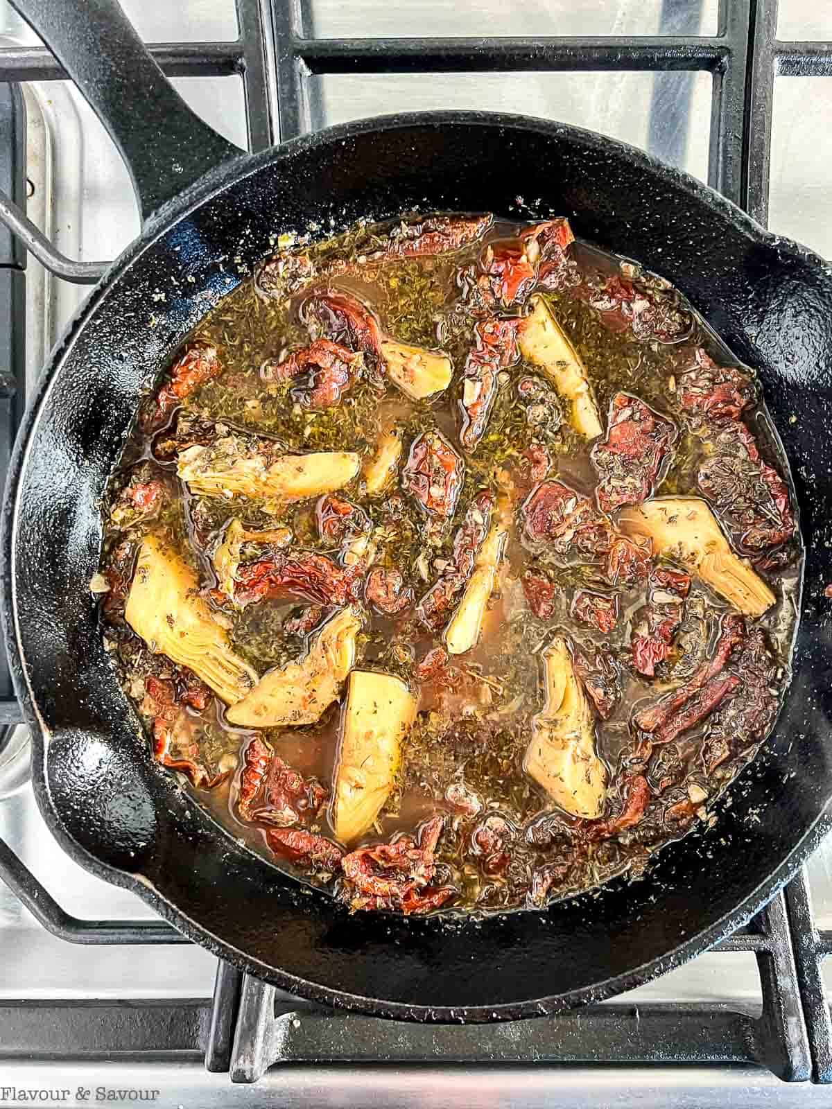 A cast iron pan with garlic, tomatoes, artichokes, wine and herbs.