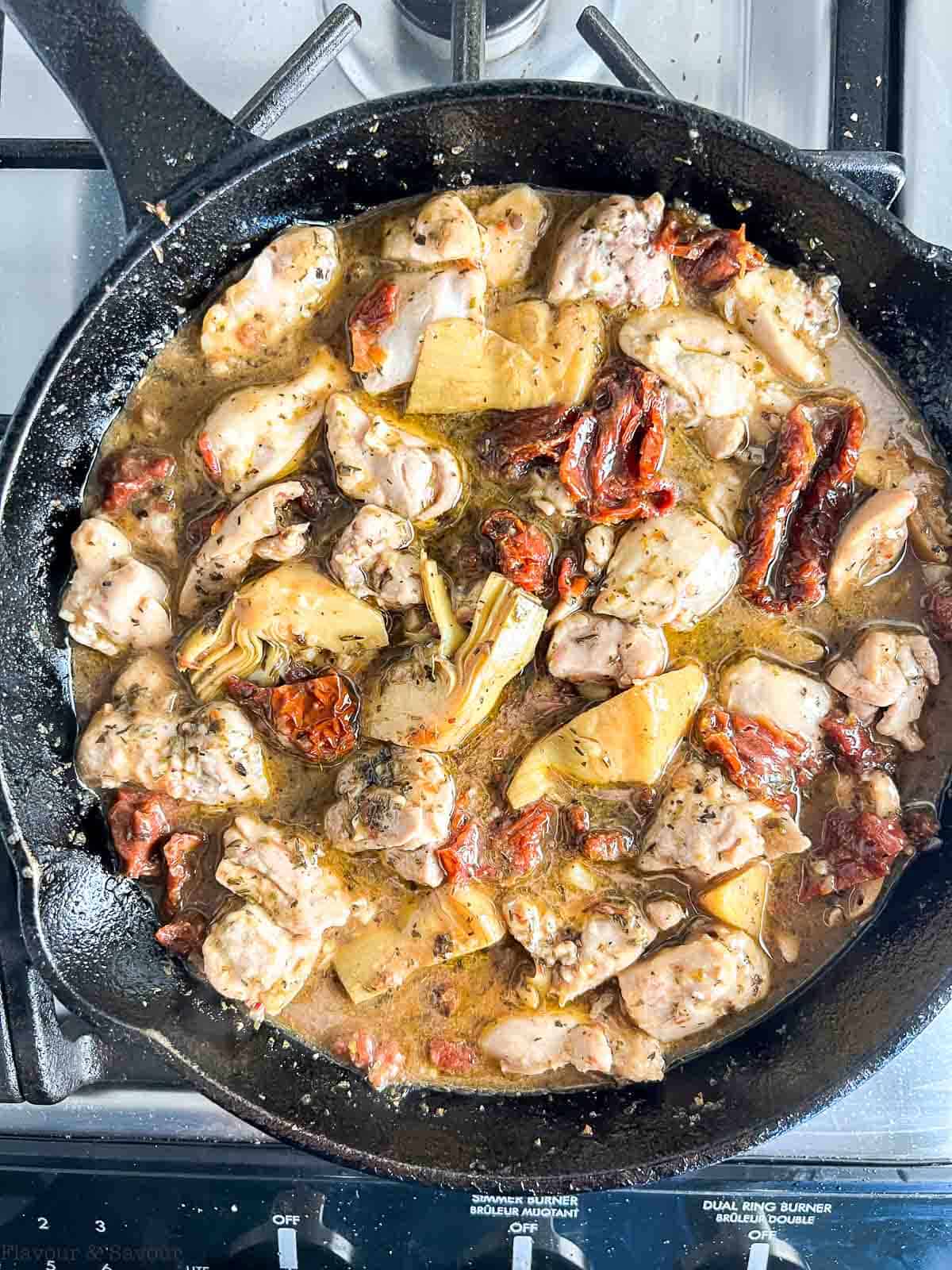 Simmering sun-dried tomato and artichoke chicken in a skillet.