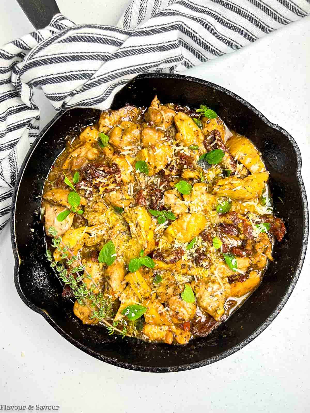 Tomato and artichoke chicken in a skillet with melted parmesan cheese.