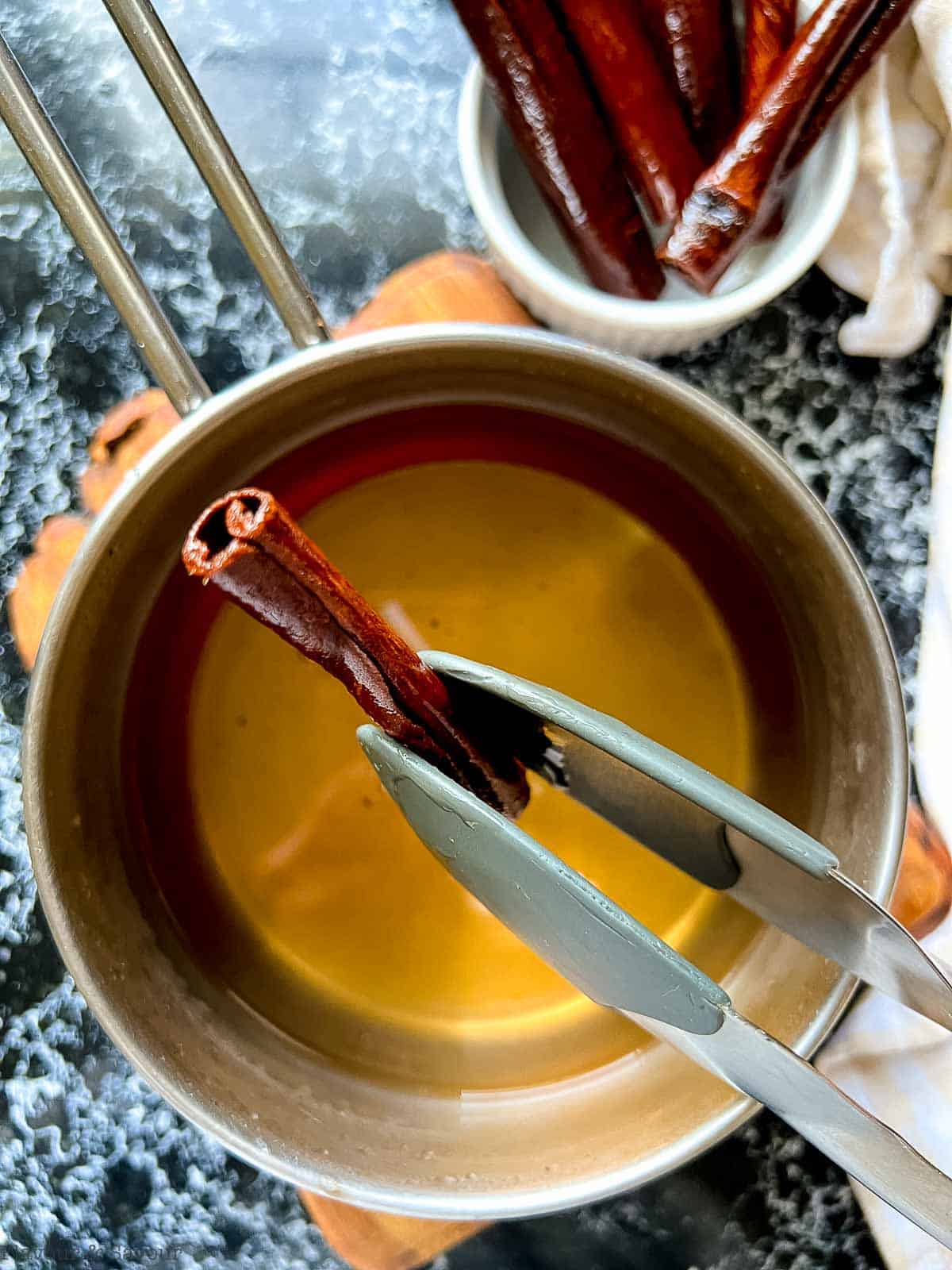 Removing a cinnamon stick from cinnamon simple syrup with tongs.