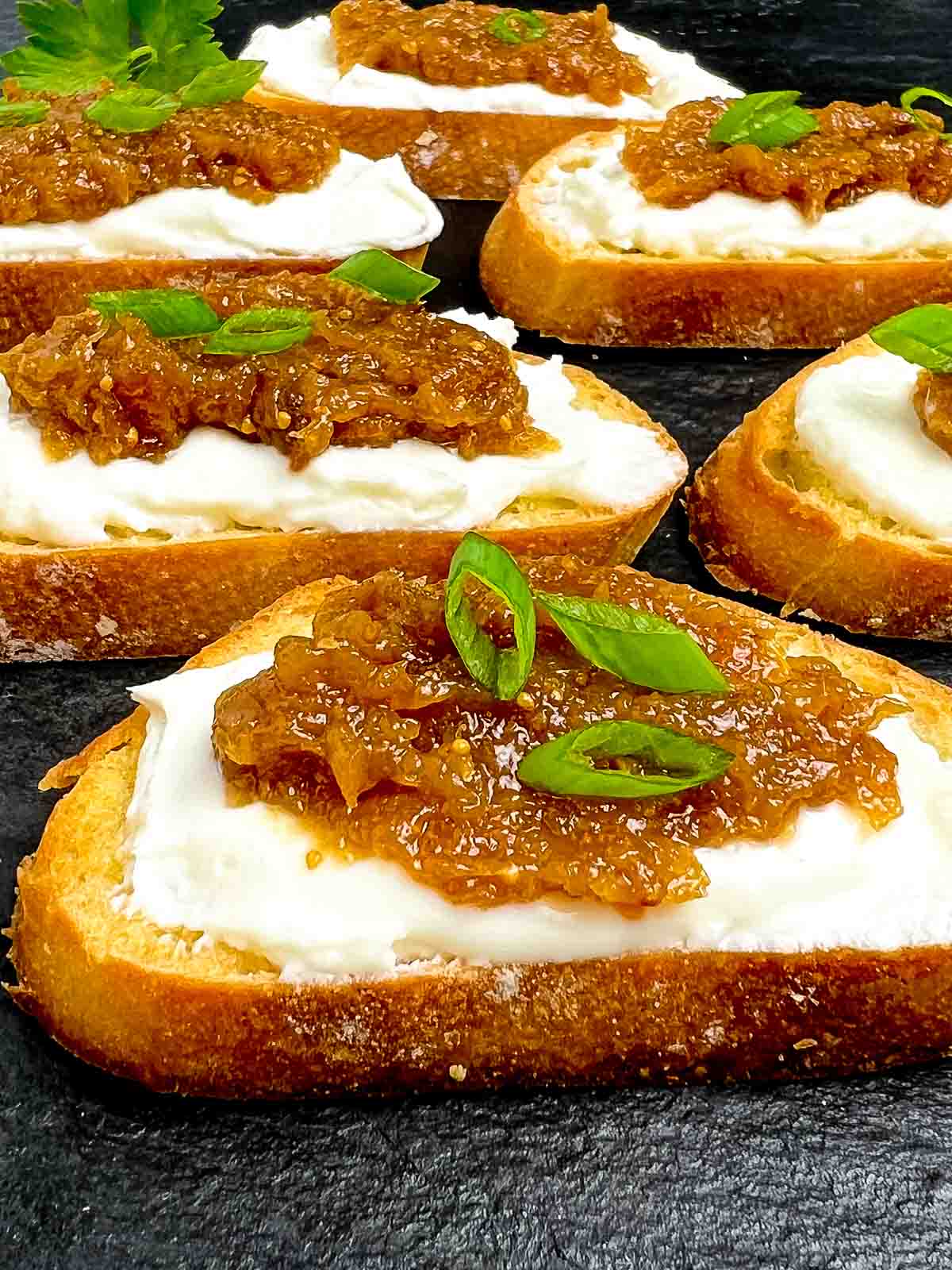 Close up view of a fig and goat cheese crostini garnished with green onion.