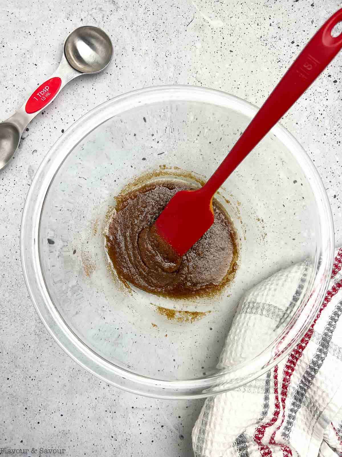 Glaze for pretzel and nut snack mix in a glass bowl with a spatula.