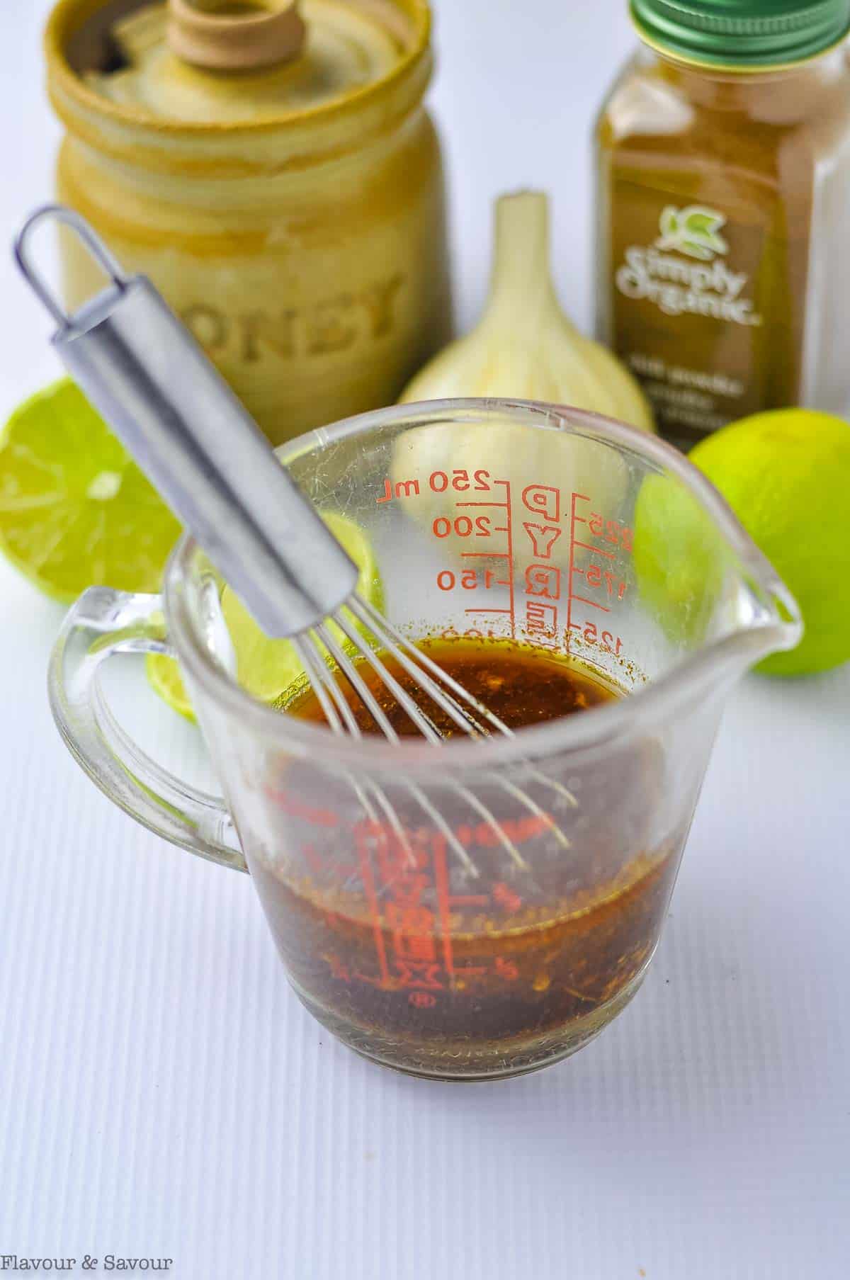 Whisking ingredients for honey lime chili chicken thighs in a glass measuring cup.