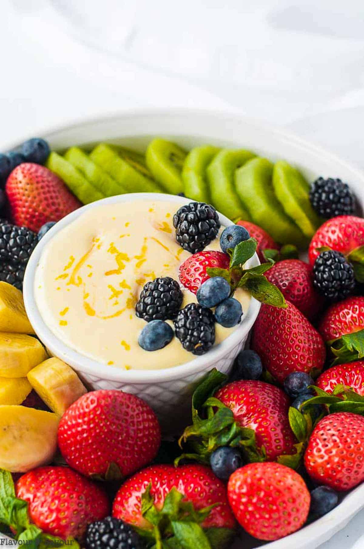 Berries, kiwi and banana slices with a bowl of lemon curd fruit dip.