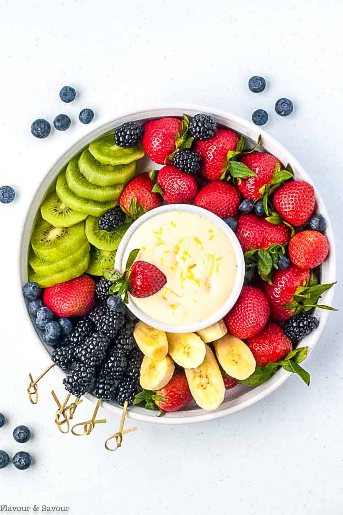 Overhead view of a round dish filled with fruit with a bowl of lemon dip in the center.